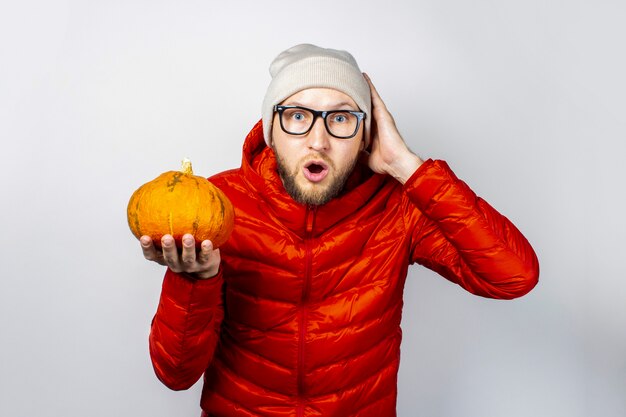 Scared young man in a red jacket, hat, holds a pumpkin and hold his hand to his head