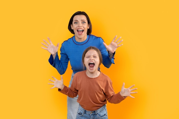 Photo scared young mother and little daughter screaming on yellow background