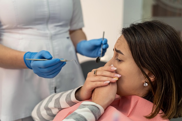 Photo scared young woman closes her mouth with her hands at the dentists appointment