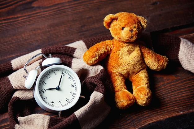 Scarf and alarm clock with teddy bear on wooden table