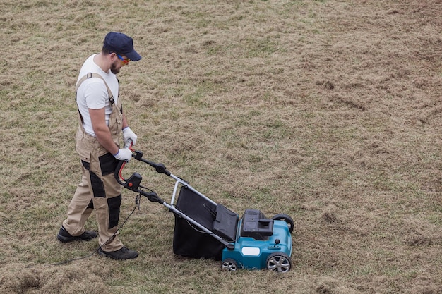 Scarifying lawn with scarifier Man gardener scarifies the lawn and removal of old grass