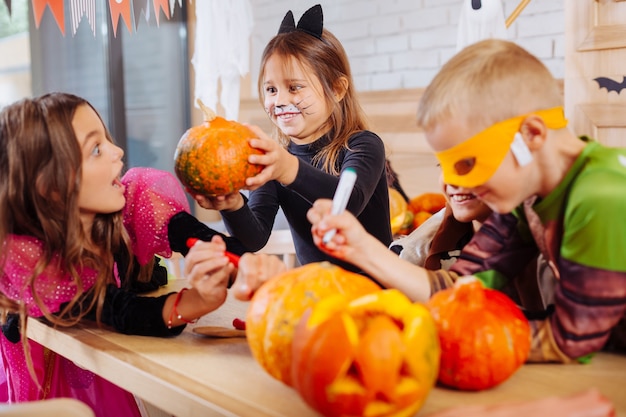 Amico spaventoso. carina ragazza dai capelli scuri con la faccia dipinta di gatto che spaventa i suoi amici che celebrano halloween insieme