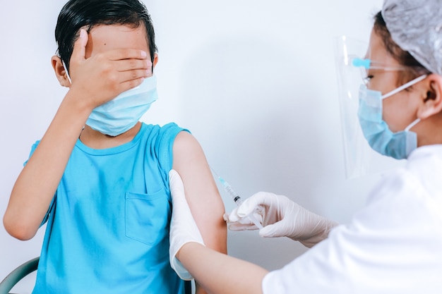 医者によるワクチン注射中の怖い男の子の表情、注射恐怖症。