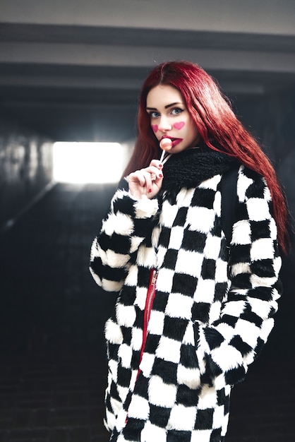 Scary dare Girl stands near subway tunnel with clown style make-up for Halloween