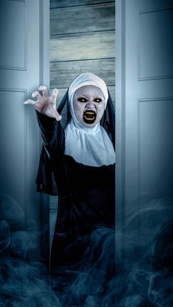 A scary devil nun standing on the open door and white smoke with a wooden wall background Scary woman Halloween concept