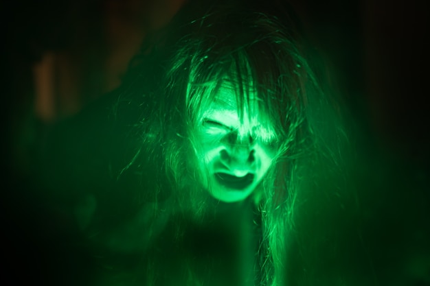 Scary ghost woman screaming through dirty glass on dark background