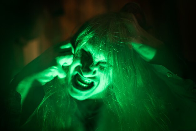 Scary ghost woman screaming through dirty glass on dark background