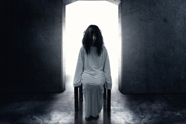 Страшная призрачная женщина с кровью и грязным лицом сидит в темной комнате