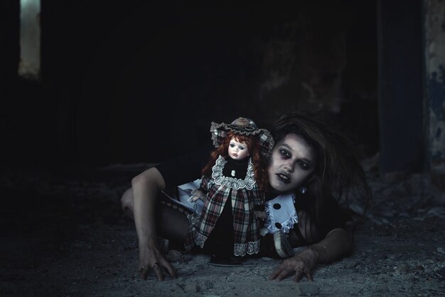 A scary girl with a doll on the floor in an abandoned house.an idea for halloween