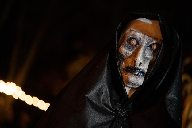 Photo scary halloween witch with red eyes in a black cloak in a gloomy environment