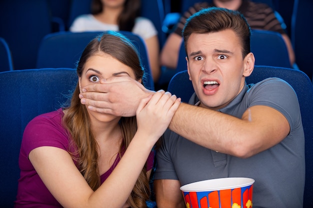 Scary moment. Shocked young couple watching a scary movie together while sitting at the cinema