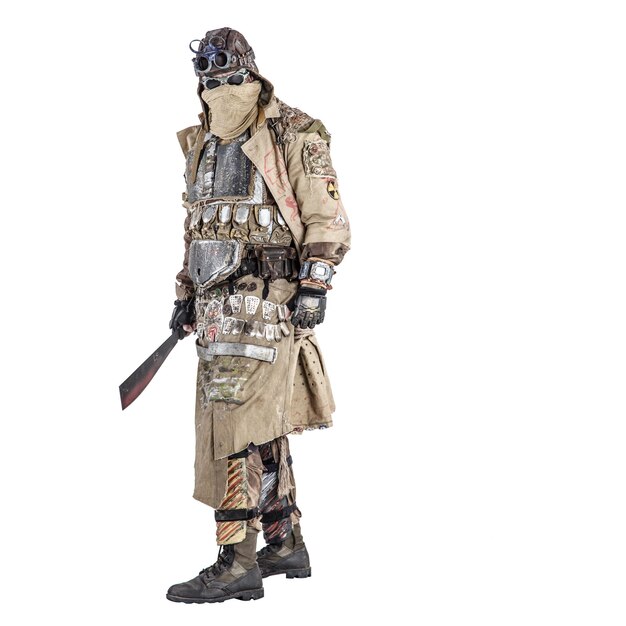 Photo scary post apocalyptic survivor in handmade armored clothes armed with machete dangerous creature with face hidden behind mask and glasses in rags standing with cold weapon in hand studio shoot