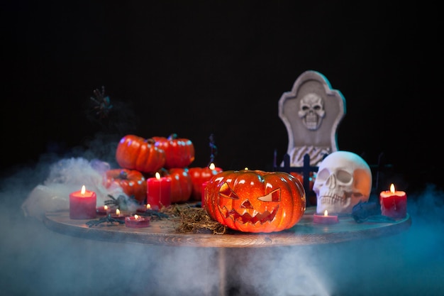 Photo scary pumpkin and creepy skull sitting together on a wooden table at halloween party. halloween smoke. haunted headstone.