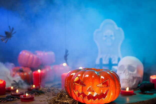 Scary pumpkin for halloween surrounded by mist on a wooden table. Burning candles.