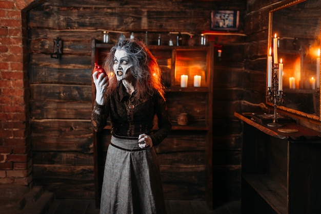 Photo scary witch holds human heart at the mirror and candles, dark powers of witchcraft, spiritual seance. female foreteller calls the spirits, terrible future teller