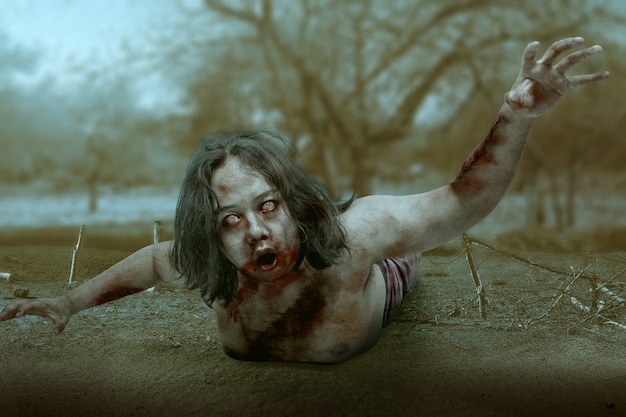 Photo scary zombie with blood and wound on his body crawling on the field