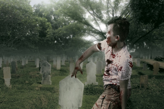 Zombie spaventoso con sangue e ferita sul corpo che cammina sul cimitero