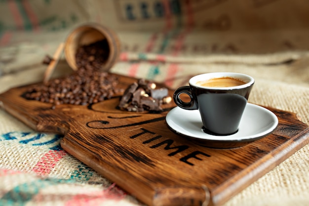 Scattered coffee beans, a cup of espresso, pieces of chocolate with nuts on a wooden board.