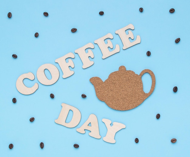 Scattered coffee beans a teapot and the inscription coffee day on a blue background The concept of a popular invigorating drink