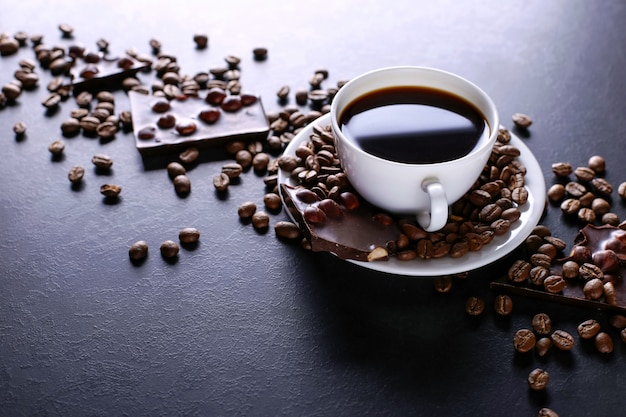 검은 돌 테이블에 흩어져있는 커피 곡물, 컵과 블랙 초콜릿. 공간을 복사하십시오.