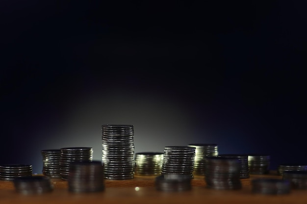 Фото Рассеянные кучи монет на деревянной доске с задним освещением очертили башню, экономя деньги и экономию