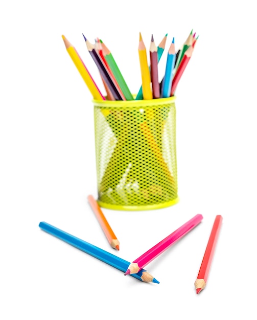 Scattered colored pencils with green metal holder with colored pencils on white background
