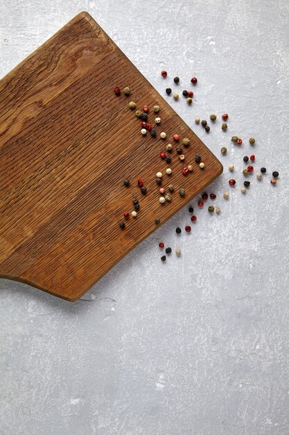 Scattered colorful peppercorns on a brown wooden cutting board on a gray concrete table Template for displaying food Top view with copy space