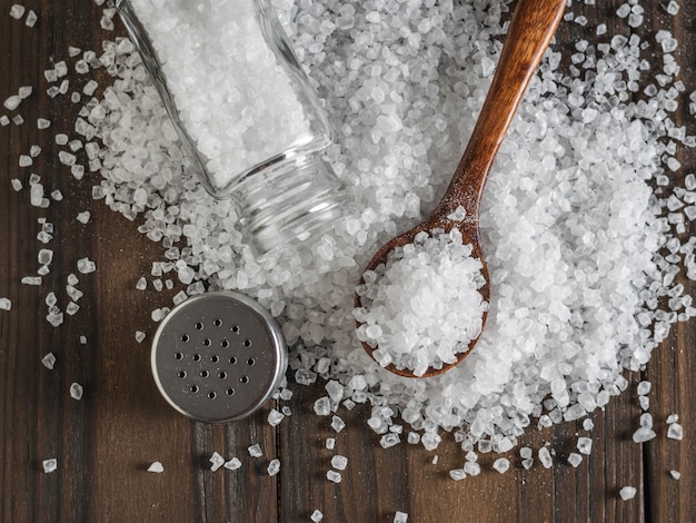 Scattered large sea salt with a wooden spoon and salt shaker. Ground stone sea salt.