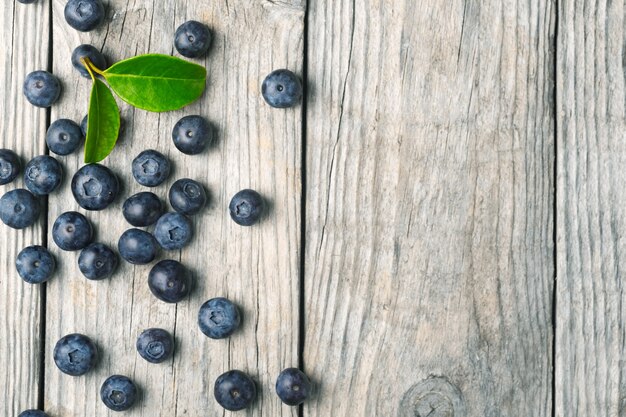 Scattered organic blueberries with leaves on wooden background