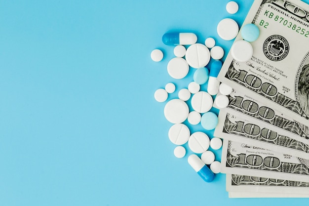 Pillole, compresse e capsule sparse della medicina farmaceutica sui soldi del dollaro isolati su fondo blu