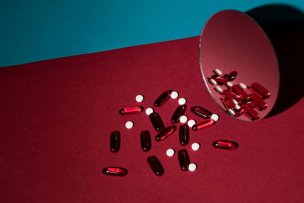 Разбросанные таблетки на красно-синем фоне с зеркалом