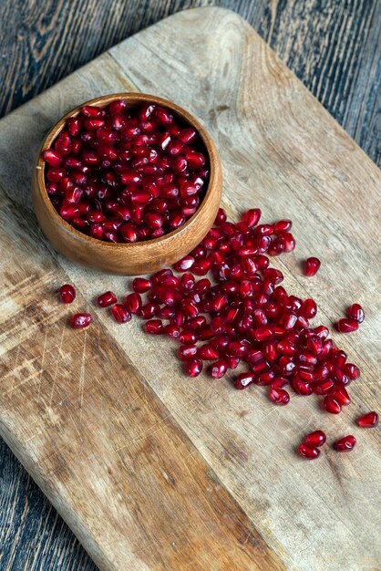 Scattered pomegranate seeds on a wooden board red ripe pomegranate seeds are scattered on a wooden cutting board