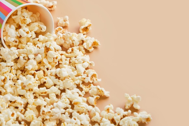 Popcorn sparsi da un bicchiere di carta a strisce di carta su una superficie giallo pastello