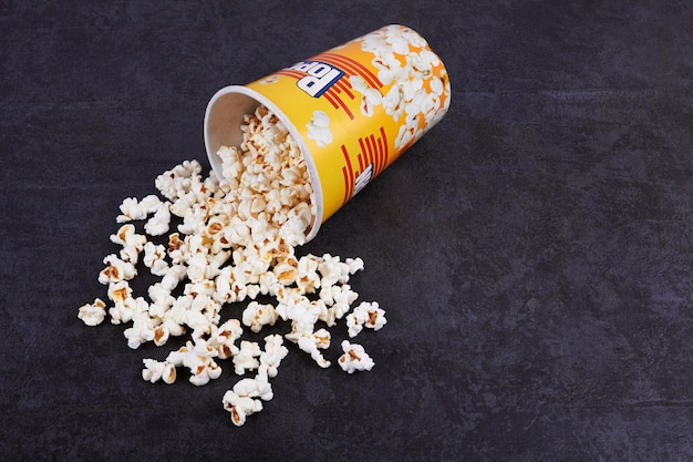 Photo scattered popcorn from yellow bucket on dark background