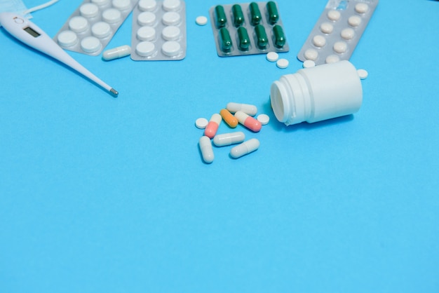 Scattered white pills on blue table.Medical, pharmacy and healthcare concept. Blue background white pills with a medical statoscope, top view.