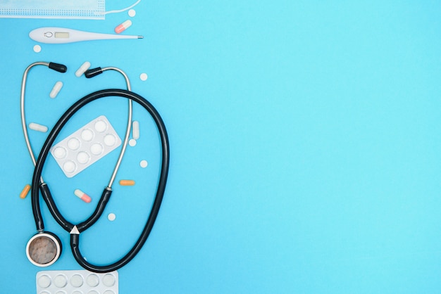 scattered white pills on blue table.medical, pharmacy and healthcare concept. blue background white pills with a medical statoscope, top view.