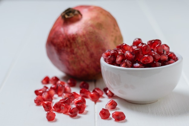 Scattered on a white table pomegranate seeds and ripe pomegranate. Vegetarian food.