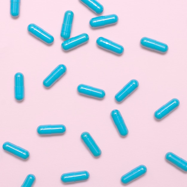 A scattering of blue pills on a pink background