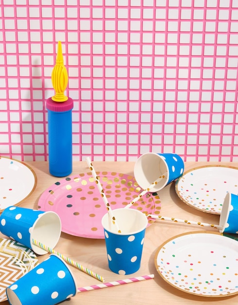 Scene from a happy birthday party Festive colored blue paper cups with straws and different plates scattered on the table Balloon air pump stands near beautiful wall