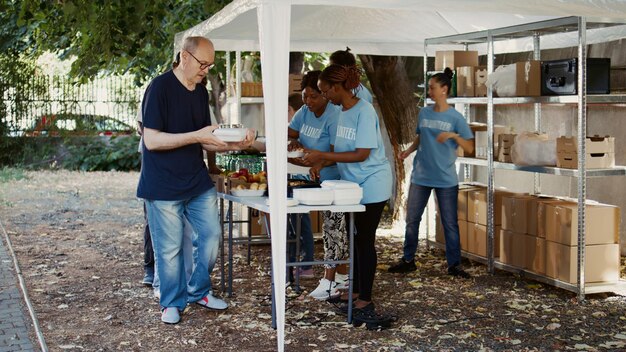 Photo scene showcasing group of volunteers giving food donations to less privileged young voluntary individuals volunteering their time to help the needy and provide homeless people free meals handheld