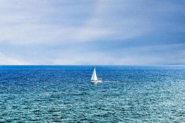 Scene of a small boat with sail in the middle of the blue ocean.