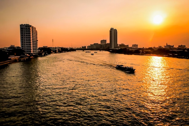 Scène van de prachtige bezienswaardigheden van de Chao Phraya-rivier met een lange staartboot en rondbouwen. Ervaar het exotische Bangkok bij zonsondergang. Mooie oranje lucht. Vanaf de brug de rivier oversteken