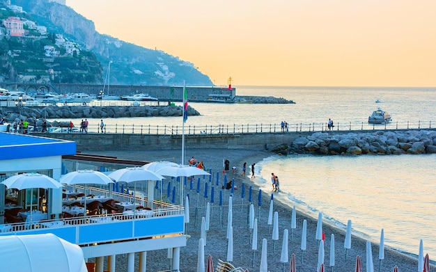 Scenery of cafe and Beach on Amalfi coast town at Tyrrhenian sea in autumn. Restaurant with table and chairs on Amalfitana coastline in Italy. Italian summer with blue water. Holiday and vacation