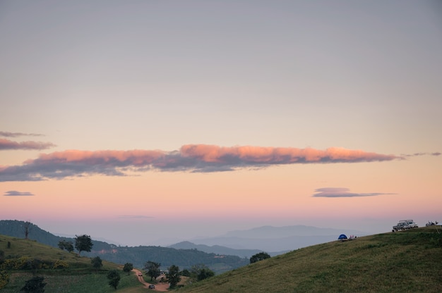 国立公園での夕方の色とりどりの空と観光テントのある緑の丘の風景