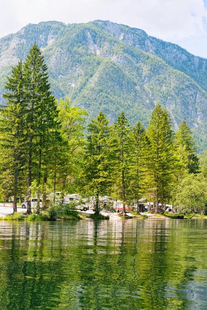 Scenery with camping of RV caravan trailers at Bohinj Lake in Slovenia. Nature and camper motorhomes in Slovenija. View of motor home van and green forest. Landscape in summer. Alpine Alps mountains