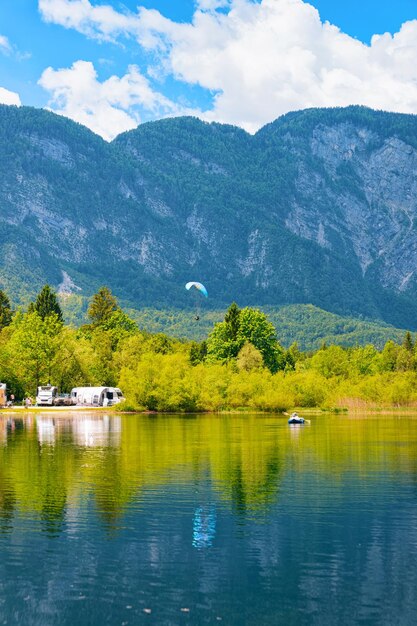 Premium Photo | Scenery with camping of rv caravan trailers, people paragliding and canoe at bohinj lake in slovenia. nature and camper motorhomes in slovenija. view of motor home van and mountains. Premium Photo | Scenery with camping of rv caravan trailers, people paragliding and canoe at bohinj lake in slovenia. nature and camper motorhomes in slovenija. view of motor home van and mountains.