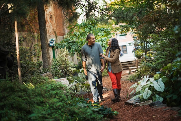 Сцены из городской жизни в Нью-Йорке. Мужчина и женщина, пара, прогуливающаяся по парку через зеленое пространство с деревьями, зеленой листвой и скамейкой.