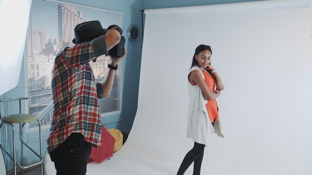 Behind the scenes on photo shoot: professional photographer working in studio by taking photos of black model