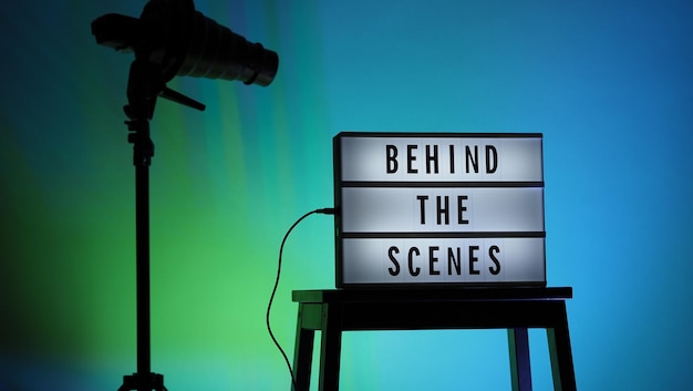 Behind the scenes text on Lightbox or Cinema Light box. Movie board light box on studio stair and light Snoot tripod on colors gradiant Background. Represent behind the scenes team is working on.