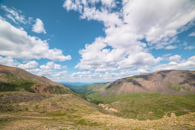 Scenic aerial view from mountain pass to green forest valley among mountain ranges and hills on horizon at changeable weather Green landscape with sunlit mountains under cumulus clouds in blue sky